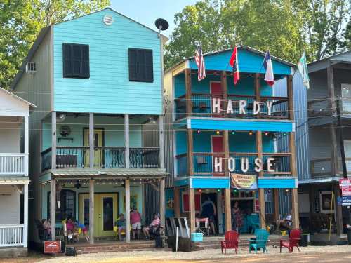 Colorful multi-story buildings with balconies, flags, and a sign reading "Hardy House," bustling with people outside.