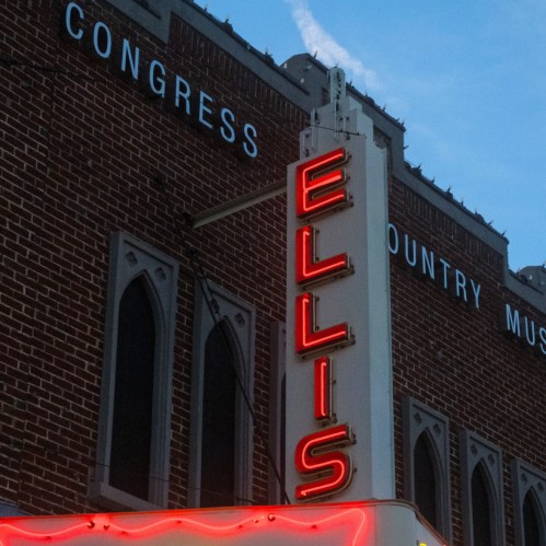 Neon sign reading "ELLIS" on a brick building, with a blue sky in the background.