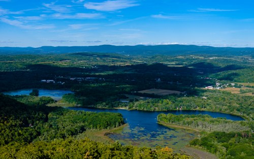 A scenic view of rolling hills and a winding river surrounded by lush greenery under a clear blue sky.