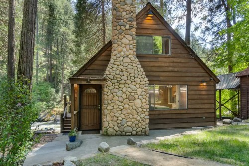 A charming wooden cabin with a stone chimney, surrounded by tall trees and a serene outdoor setting.