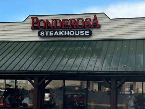 Sign for Ponderosa Steakhouse on a building with a green roof and clear blue sky in the background.