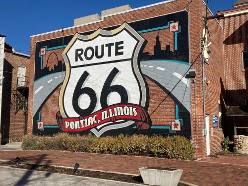 Mural of Route 66 on a brick wall in Pontiac, Illinois, featuring a highway sign and city skyline.