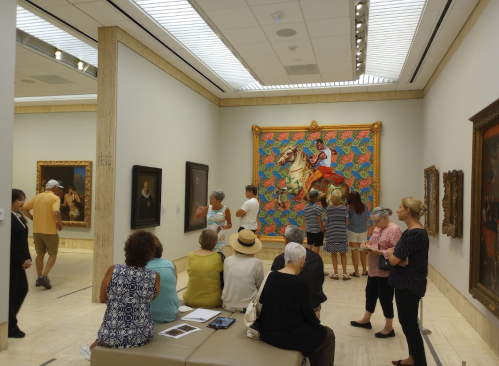 Visitors admire colorful artwork in a gallery, surrounded by various paintings and sculptures.