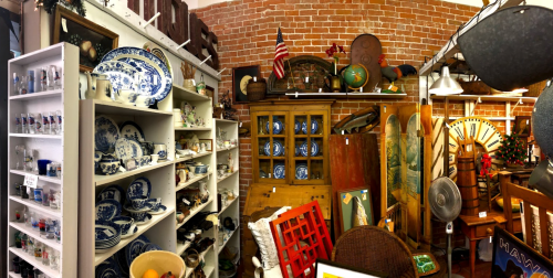 A cozy antique shop filled with vintage items, including dishes, globes, and decorative pieces against a brick wall.