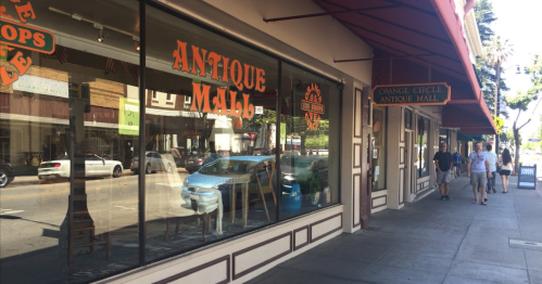 A street view of an antique mall with large windows, showcasing the storefront and pedestrians walking by.