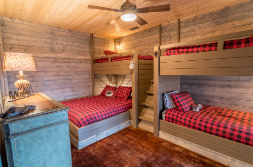 Cozy cabin bedroom with two bunk beds, plaid bedding, wooden walls, and a rustic lamp.