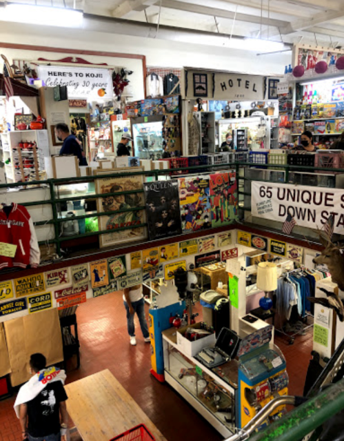 A vibrant indoor market with multiple levels, featuring vintage signs, clothing, and various unique items for sale.