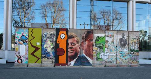 A colorful mural on a concrete wall featuring abstract designs and portraits, including a depiction of John F. Kennedy.