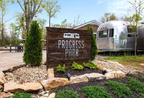 Sign for Progress Park, an Airstream resort in Louisville, KY, with greenery and an Airstream trailer in the background.
