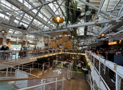 A spacious, modern restaurant interior with high ceilings, greenery, and a lively atmosphere filled with diners.