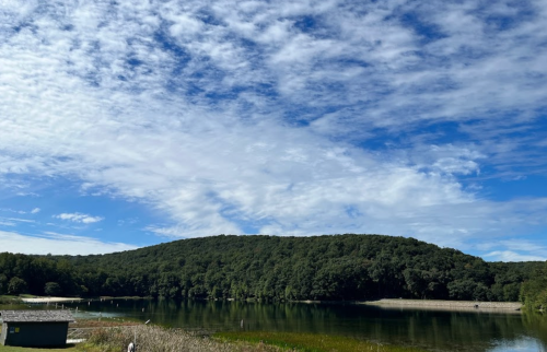 A serene lake surrounded by lush green hills under a partly cloudy blue sky.