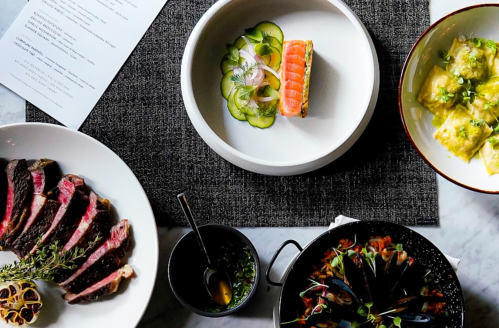 A top-down view of a dining table featuring various gourmet dishes, including steak, salmon, and pasta.
