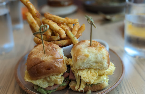 Two breakfast sandwiches with eggs and greens, served with a side of crispy fries in a bowl.