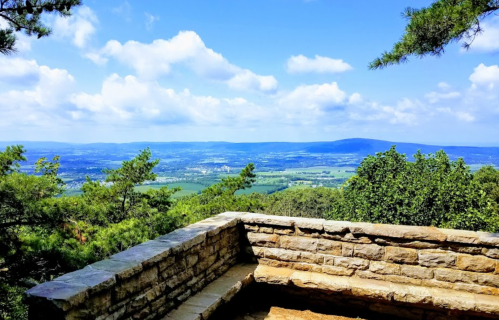 A scenic view from a stone overlook, showcasing rolling hills and a blue sky with fluffy clouds.