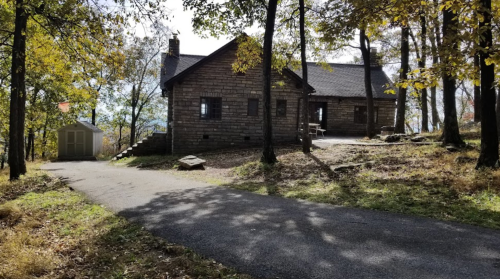 A stone house surrounded by trees, with a gravel path leading up to it and a small shed nearby.