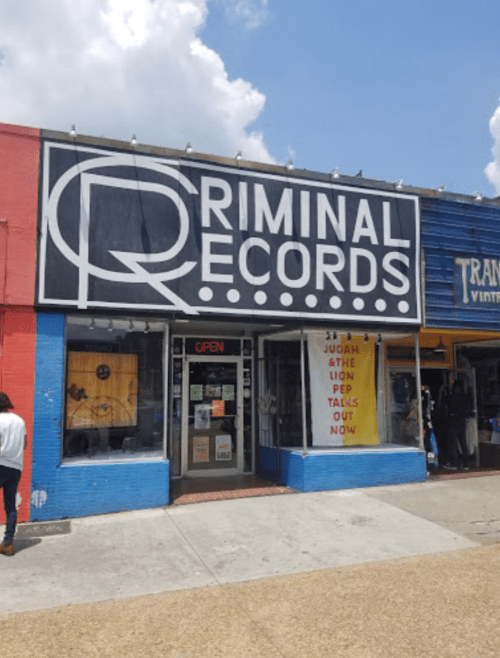 Storefront of Criminal Records with a large sign, open door, and colorful window displays.