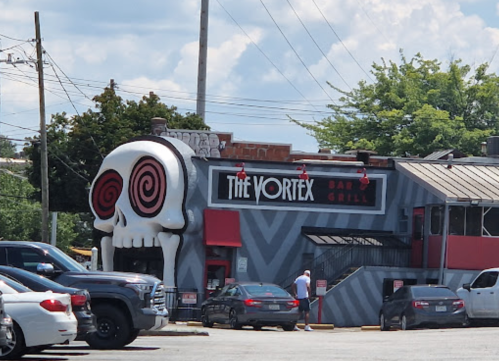 Exterior of The Vortex Bar & Grill, featuring a large skull entrance and vibrant signage against a cloudy sky.