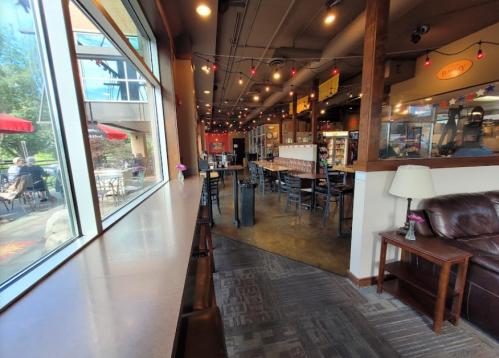 Cozy café interior with a long counter, seating area, and large windows overlooking an outdoor patio.