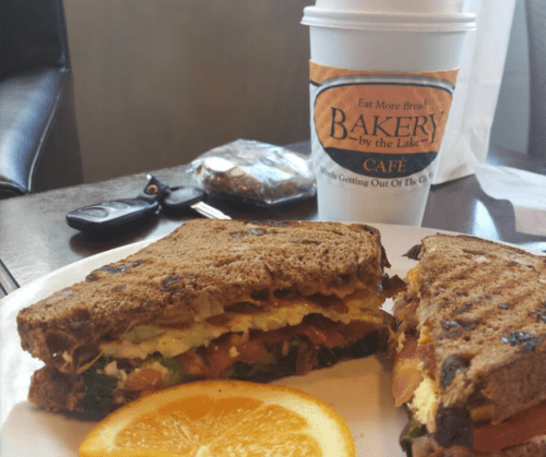 A plate with a sandwich made of whole grain bread, filled with vegetables, and a cup of coffee beside it.
