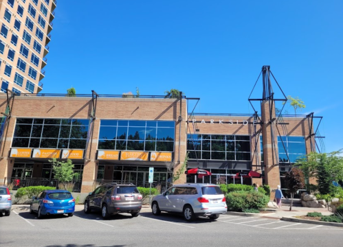 A modern brick building with large windows, featuring signs for various businesses, under a clear blue sky.