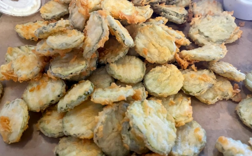 A pile of crispy, fried pickles on a brown paper surface.