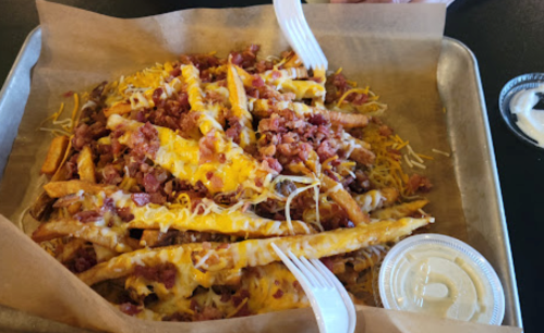 A tray of loaded fries topped with cheese, bacon bits, and served with a side of ranch dressing.