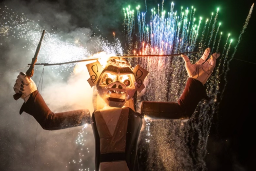 A large puppet figure with fireworks in the background, creating a dramatic and festive atmosphere.