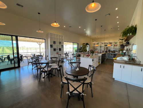 A bright, modern café interior with wooden tables, chairs, and large windows overlooking a scenic view.