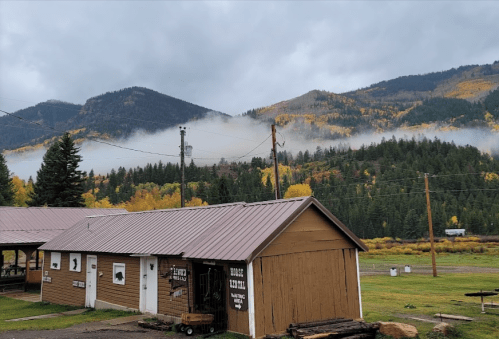 A rustic building in a mountainous landscape, with fog and autumn foliage in the background.