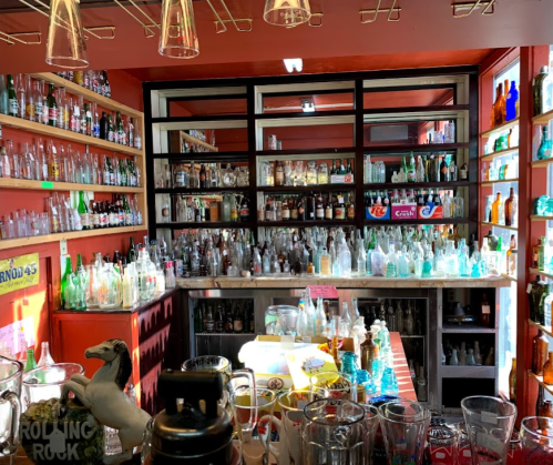 A colorful display of various glass bottles and jars on shelves and a counter in a cozy shop interior.
