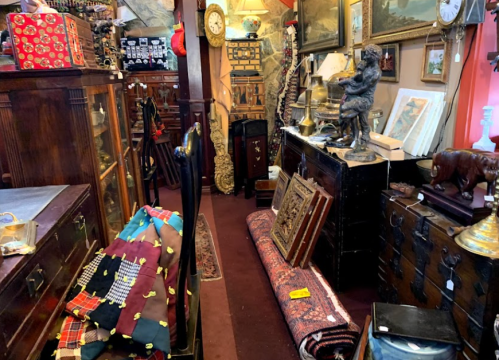 A cozy antique shop filled with various vintage items, including furniture, art, and textiles, creating a nostalgic atmosphere.