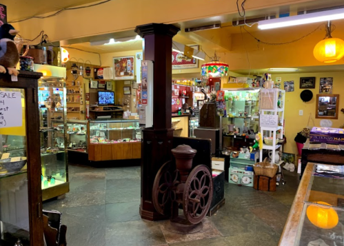 A cozy antique shop filled with various collectibles, displays, and vintage decor, featuring a large wheel in the foreground.