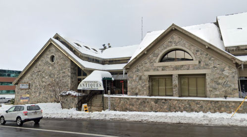 A stone building with a sloped roof, covered in snow, featuring a sign for "The Heritage Antiques."
