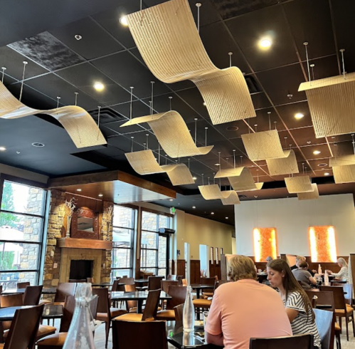 Interior of a restaurant featuring unique ceiling designs, wooden furniture, and a cozy fireplace.