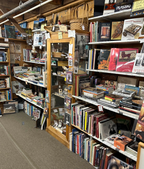A cozy bookstore interior filled with shelves of books, a display case, and various literary items.
