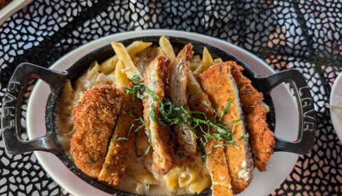 A sizzling dish of baked pasta topped with crispy chicken slices and garnished with fresh herbs.