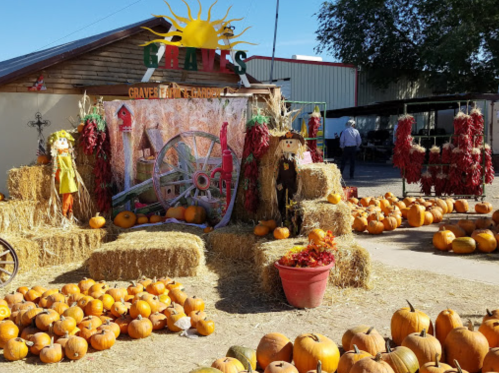 A festive pumpkin patch with hay bales, scarecrows, and a colorful backdrop featuring a sun and wheel decoration.