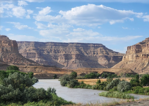 A serene river flows through a canyon landscape, surrounded by lush greenery and rocky cliffs under a blue sky.