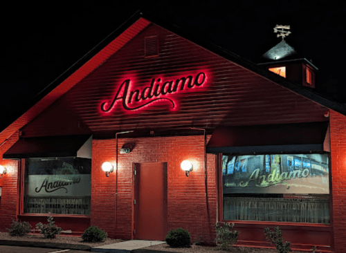 A red brick restaurant exterior at night, featuring a glowing "Andiamo" sign and illuminated windows.