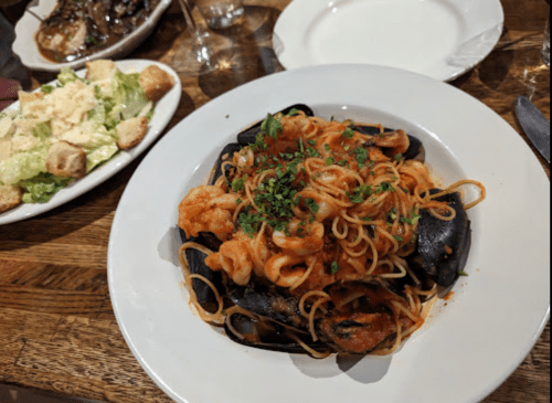 A plate of seafood pasta with shrimp and mussels, garnished with herbs, alongside a Caesar salad.