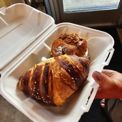 A hand holding a takeout container with a croissant and a pastry topped with almonds.