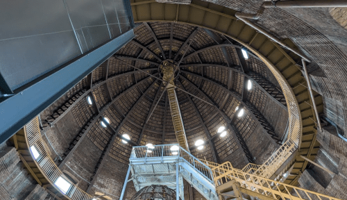 View of the interior dome of a large structure, featuring a spiral staircase and industrial beams.