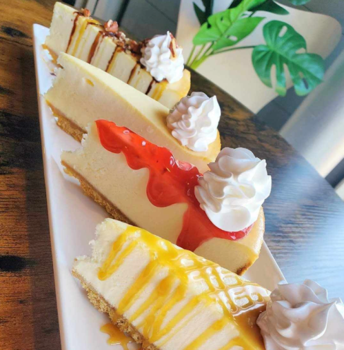 A platter of assorted cheesecakes topped with whipped cream and fruit sauces, showcasing vibrant colors and textures.