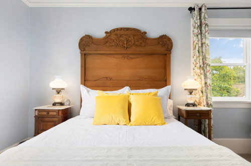 Cozy bedroom featuring a wooden headboard, yellow pillows, and floral curtains with bedside lamps.