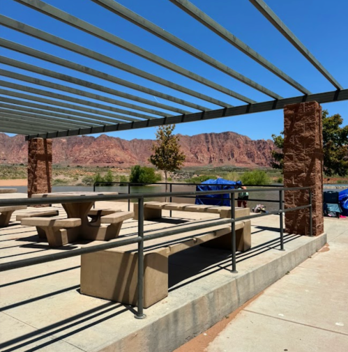 A shaded picnic area with benches and tables, overlooking red rock formations and a clear blue sky.