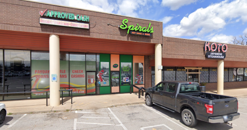 Exterior view of a shopping plaza featuring "Spirals Hot Dogs & More" and "Koto Japanese Steakhouse," with a parked truck.
