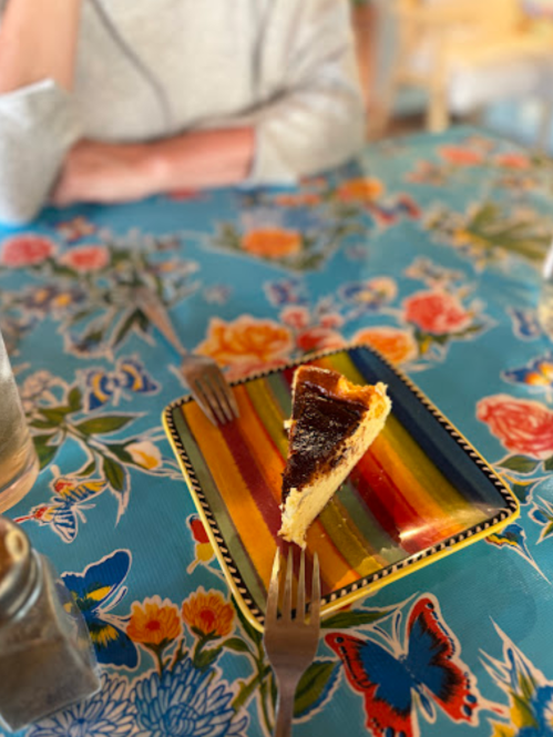 A slice of chocolate cake on a colorful plate, with forks on a vibrant floral tablecloth.