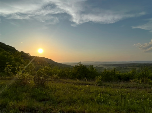 A serene sunset over rolling hills, with vibrant colors illuminating the sky and lush greenery in the foreground.