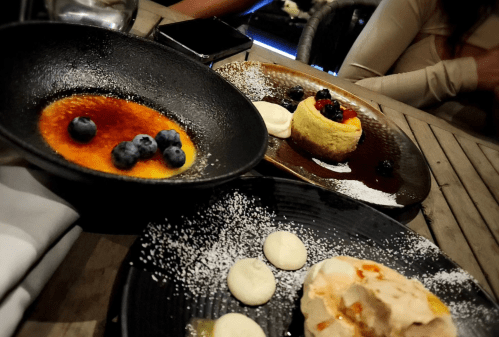 Three elegant dessert plates featuring crème brûlée, a cheesecake with berries, and a meringue dessert, garnished with powdered sugar.