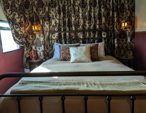 Cozy bedroom with a wrought iron bed, decorative pillows, and elegant patterned curtains. Warm lighting adds charm.